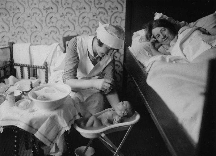 Een verpleegster doet een baby in bad bij het kraambed van een vrouw, 1928. (Beeld: Collectie Stichting Nationaal Museum van Wereldculturen)