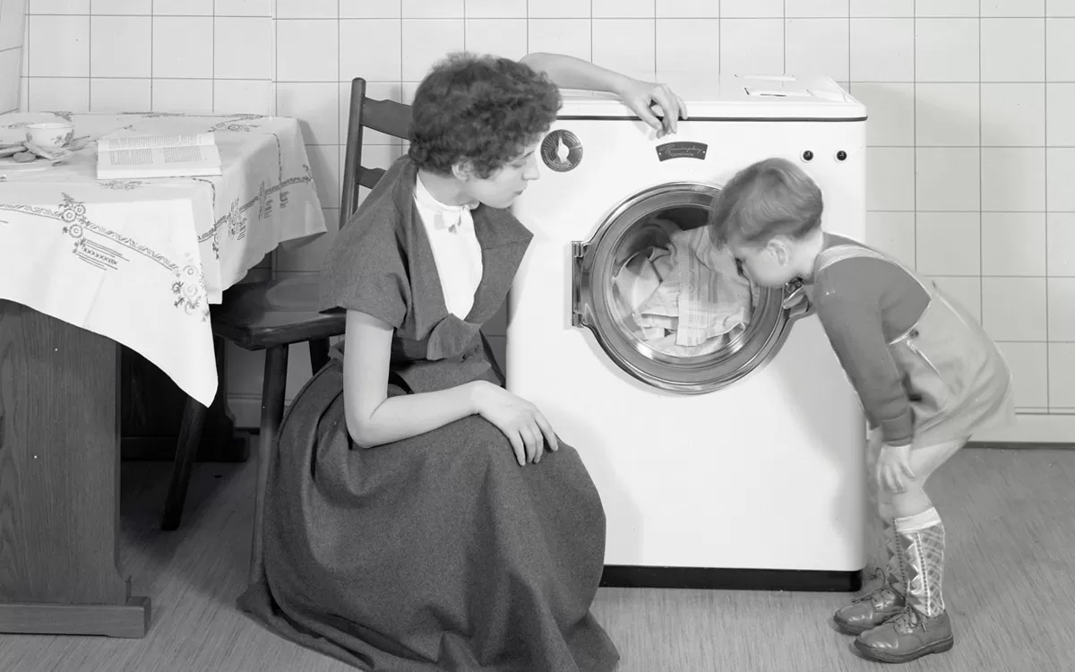 Een moeder met haar zoon bij een wasmachine, jaren vijftig. Het aantal gezinnen met wasmachine in Nederland groeide van 20% in 1955 tot 83% in 1964. (Beeld: Constructa)